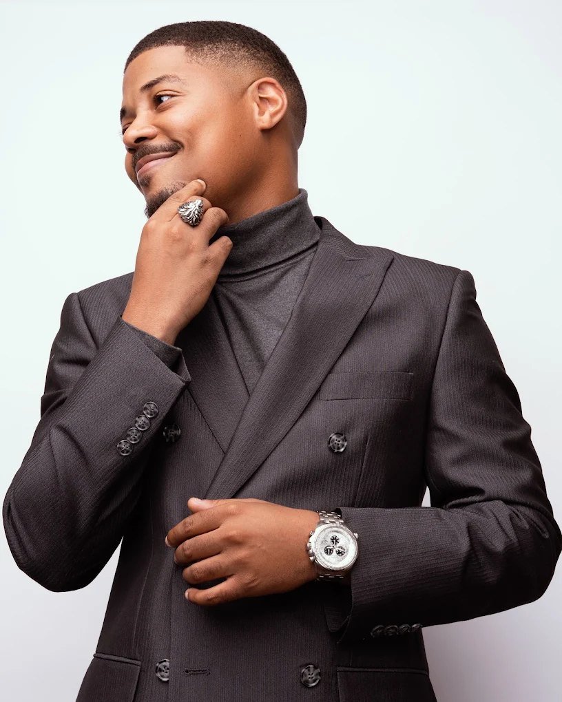 Darius Tuff in a tailored double-breasted suit and turtleneck, sharply groomed