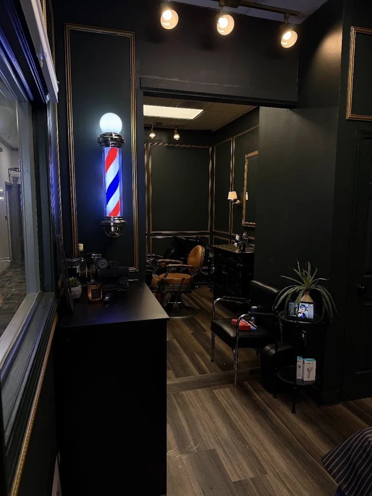 Inside The Reynard's Den with a lit barber pole, dark walls with gold trim and a cognac barber chair