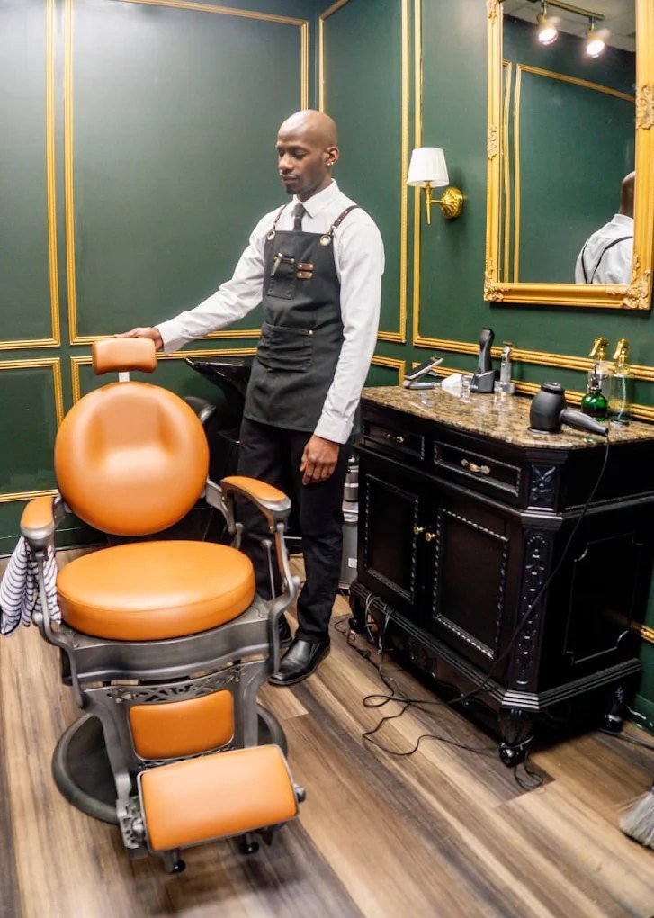 Barber Kevin Black standing beside the cognac leather barber chair